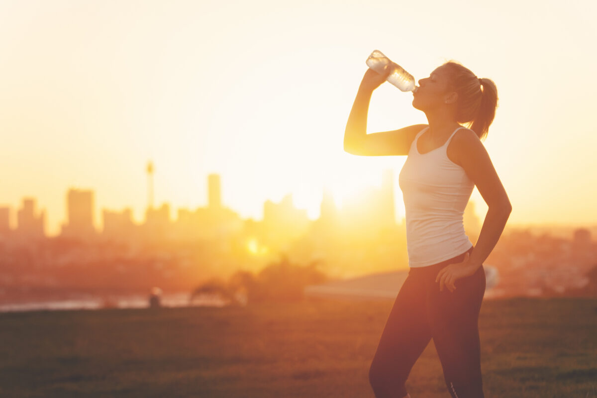 Woman drinks water in front of city skyline at sunset